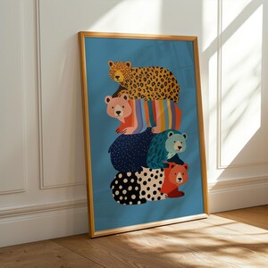 May include: A framed art print showing a stack of colourful bears on a teal background. The bears have various patterns, including leopard print, polka dots, and stripes. The frame is a light brown colour.