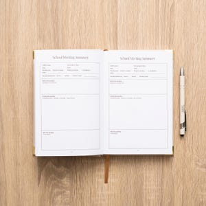 May include: An open planner with white pages featuring the printed text School Meeting Summary. The layout includes sections for Child's name, Date, Time, and meeting details. A silver pen with a black grip is positioned to the right of the planner.
