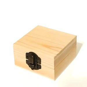 May include: A small, square wooden box with a hinged lid and a brass latch. The box is made of light-colored wood and has a smooth finish.