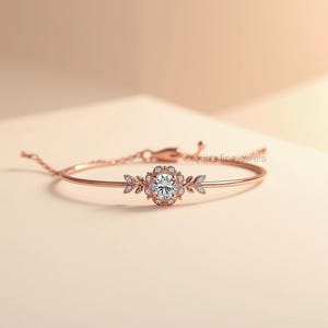 May include: Rose gold bracelet featuring a central floral design with a large, clear gemstone surrounded by smaller stones. Delicate leaf accents flank the central design. The bracelet is a delicate piece of jewelry.