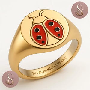 Può includere: Anello a sigillo color oro con un design a coccinella rossa e nera. L'anello ha una finitura liscia e lucida e il testo "SILVERJEWELLERYGEMS" è inciso sulla fascia. Un gioiello.