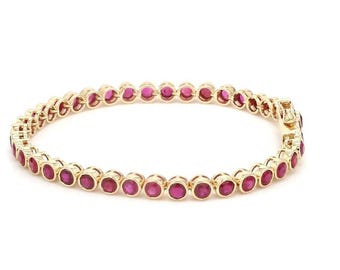 May include: A gold-toned bracelet featuring a series of round, vibrant red gemstones. The gemstones are set closely together, creating a continuous line around the wrist. The bracelet has a secure clasp.