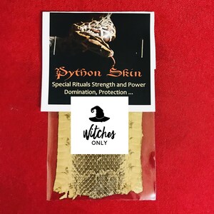 Pode incluir: Um pacote de pele de píton com um rótulo que diz "Python Skin" e "Special Rituals Strength and Power Domination, Protection...". O pacote também tem um rótulo menor que diz "Witches ONLY" com um gráfico de chapéu de bruxa. O fundo é vermelho.