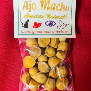 Puede incluir: Una bolsa de plástico transparente llena de dientes de ajo secos. Una etiqueta blanca con el texto "Ajo Macho" y "Amulet Natural!" está adherida a la bolsa. El fondo es de color rojo liso.