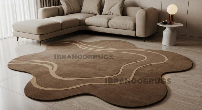 May include: A brown, abstract-shaped rug with a lighter brown wavy design. The rug is on a tiled floor in front of a beige sectional sofa. The text "IBRANOORRUGS" is printed on the rug.