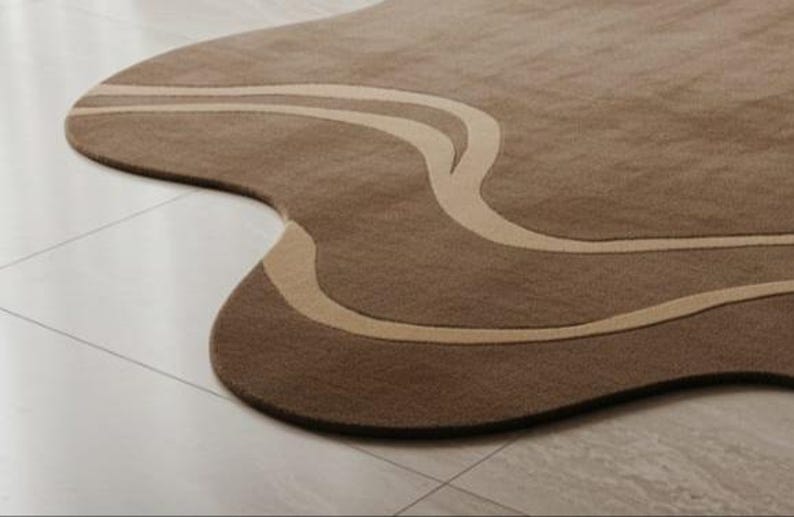 May include: A brown area rug with a unique, organic shape. The rug features a lighter beige, flowing design across its surface. The rug is placed on a light-colored tile floor, adding a touch of modern design to any space.