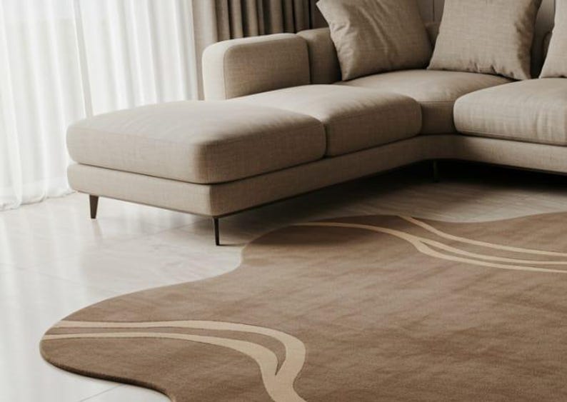 May include: A modern living room scene featuring a beige sectional sofa and a uniquely shaped brown rug. The rug has a wavy design with lighter beige stripes. The room is illuminated by natural light from a nearby window.