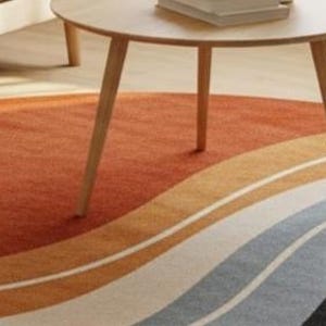 May include: A round area rug with a wave design in shades of orange, cream, gray, and black. The rug is placed on a light wood floor, with a wooden side table and a sofa visible in the background.