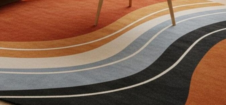 May include: A colorful area rug with a wavy design. The rug features bands of orange, brown, tan, white, gray, and black. A wooden table leg is visible in the upper portion of the image.