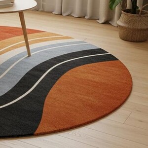 May include: A round area rug with a wave design in shades of orange, tan, gray, black, and white. The rug is placed on a light wood floor, with a small table and a woven basket in the background.