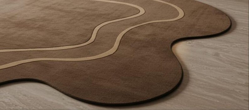 May include: A brown, uniquely shaped rug with a wavy, lighter-colored design. The rug has a dark brown border and a soft, textured surface. The design is reminiscent of a flowing river or abstract landscape, adding a modern touch to any room.
