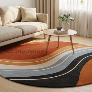 Modern abstract round tufted rug with cream base, burnt orange curves, and black accent lines placed in a mid-century modern living room with a beige sofa, wooden floor, and natural light.https://ibranoorrugs.etsy.com