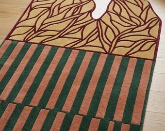 Puede incluir: Una alfombra rectangular con un diseño único. La sección superior presenta un fondo de color beige claro con un patrón de hojas burdeos. La sección media tiene rayas verdes y melocotón alternas. La alfombra está colocada sobre un suelo de madera.
