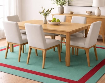 Puede incluir: Un comedor con una mesa de madera clara y seis sillas tapizadas. Una pantalla de lámpara tejida cuelga encima. La habitación incluye una alfombra verde con borde rojo, un aparador y una pintura de paisaje. La alfombra mide aproximadamente 244 cm x 305 cm.