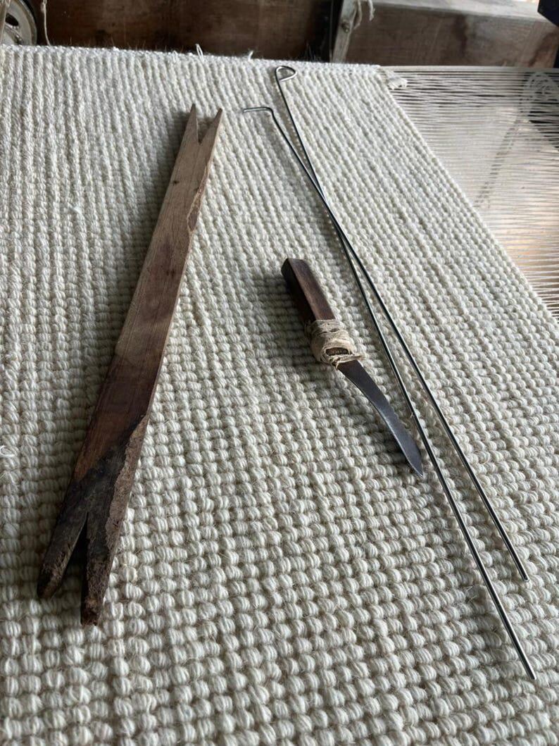 Puede incluir: Una herramienta larga y plana de madera marr&oacute;n con una muesca en forma de V en ambos extremos, un peque&ntilde;o mango de madera marr&oacute;n oscuro con una punta de metal curvada envuelta en cuerda clara, y dos varillas met&aacute;licas plateadas largas y finas.