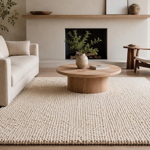 May include: A large, rectangular area rug featuring a thick, chunky knit texture in a solid off-white colour. The rug is crafted with a prominent, repeating loop pattern that creates a dense, tactile surface across the entire floor covering.