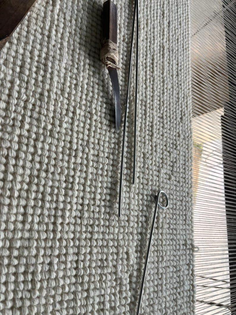 Puede incluir: Una herramienta con mango de madera marr&oacute;n oscuro y hoja de metal curva, dos varillas de metal plateado largas y delgadas, y una varilla de metal plateado con un bucle circular en un extremo, sobre una tela tejida de color blanco roto.