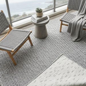 Puede incluir: Escena de patio al aire libre con dos sillas grises tejidas con marcos de madera, una alfombra a juego y una pequeña mesa auxiliar. Las plantas en macetas y una manta gris completan la estética relajante. La alfombra mide aproximadamente 200 cm por 300 cm.