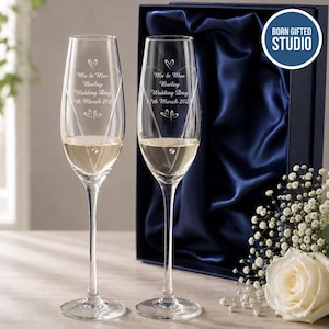 May include: Two clear glass champagne flutes with slender stems and a single embedded crystal. Each flute is engraved with a heart outline, the text Mr & Mrs Bailey Wedding Day 17th March 2025, and two small hearts. The glasses are presented in a dark blue box.