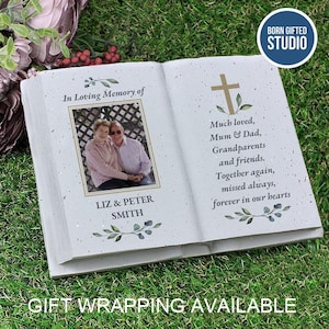 May include: A book-shaped memorial ornament with a photo of a couple, Liz and Peter Smith, and the words "In Loving Memory of." The book features a cross and the text "Much loved, Mum & Dad, Grandparents and friends." The studio logo is visible.