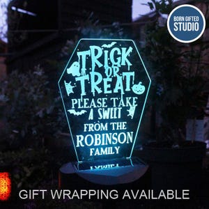 May include: A teal-lit, coffin-shaped Halloween sign with the words "Trick or Treat" and "Please take a sweet from the Robinson Family". The sign features bats, ghosts, and a pumpkin. The base is dark.
