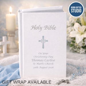 May include: A white Holy Bible with silver embossed text and a cross symbol. The cover is personalised with the text: On Your Christening Day, Thomas Carlise, St Mark's Church, 30th August 2026. The book has a textured finish and a hard cover.