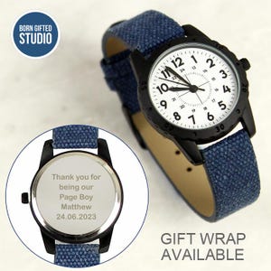 May include: A wristwatch with a black case, white dial featuring black numerals, and a textured blue fabric strap. An inset shows the watch back engraved with the text: Thank you for being our Page Boy Matthew 24.06.2023. The watch has a black bezel.
