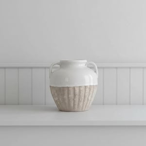 May include: A two-handled ceramic vase featuring a smooth, glossy white upper section and a textured, matte beige lower section with vertical ribbed detailing. The vessel has a wide, rounded body and a short, narrow neck with two side handles.