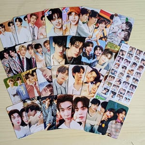 May include: A collection of K-pop idol photo cards featuring various male performers. The cards display individual portraits and group shots, with vibrant colors and glossy finishes. The cards are arranged in a fan-like display.