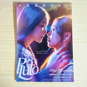 Op de afbeelding: Een boekomslag met twee vrouwen in een innige omhelzing, in een romantische sfeer, met paarse en blauwe tinten. De titel "Pluto" staat in een gestileerd lettertype. Extra tekst in een vreemde taal is ook zichtbaar.