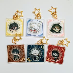 Pode incluir: Coleção de chaveiros de personagens em estilo anime. Cada chaveiro apresenta um design de personagem diferente em um pingente quadrado de acrílico, com ferragens douradas em forma de estrela. Os pingentes têm várias cores de fundo, incluindo amarelo, azul e vermelho.