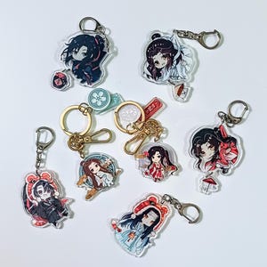 Puede incluir: Una colección de llaveros acrílicos con ilustraciones de personajes de estilo anime. Los llaveros tienen herrajes metálicos dorados y representan varios personajes con atuendos coloridos. Algunos llaveros tienen dijes adicionales.
