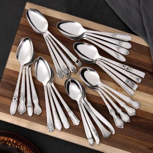 Peut inclure: Un assortiment de cuillères en argent avec des manches décoratifs, disposées sur une planche en bois. Les cuillères présentent divers motifs, notamment floraux et géométriques. Les cuillères sont très polies, et l'arrangement suggère un cadre de restauration formel.