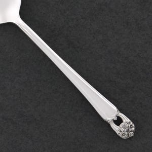 Puede incluir: Una cuchara de servir plateada con un diseño floral en el extremo del mango. La cuchara tiene un mango largo y delgado y un cuenco redondeado. La cuchara está hecha de metal brillante y reflectante, sobre un fondo oscuro.