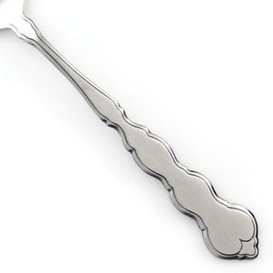 May include: A silver-toned metal spoon handle featuring a brushed finish and a scalloped, wavy edge design. The handle tapers toward the bowl of the spoon and ends in a rounded, decorative tip with a subtle embossed outline detail.