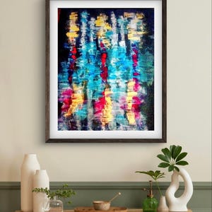 May include: Abstract art print in a dark wooden frame. The artwork features vertical brushstrokes in shades of blue, red, yellow, and pink against a dark background. The painting is displayed above a wooden table with decorative vases.