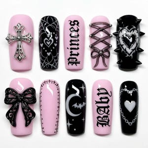 Puede incluir: Un conjunto de diez uñas artificiales con diversos diseños. Las uñas presentan bases rosas y negras, adornadas con elementos como una cruz, telaraña, lazos y las palabras "princess" y "baby".