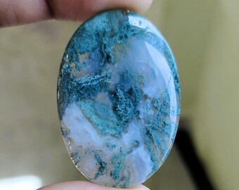 May include: An oval-shaped gemstone with a captivating blend of colors. The stone features a base of translucent white and blue, overlaid with intricate patterns of teal and green, creating a natural, artistic design. The polished surface reflects light, highlighting the stone's unique textures.