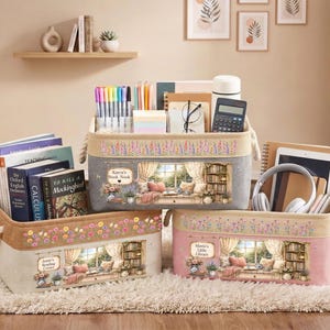 Peut inclure: Trois bacs de rangement rectangulaires en tissu avec des poignées en corde. Ils présentent une bande supérieure beige à motifs floraux et une section inférieure illustrant une bibliothèque. Les bacs portent les inscriptions Karen's Book Nook, Jamie's Reading Corner et Mavis's Little Library.