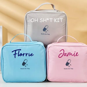 May include: Three square medicine bags in light blue, pink, and gray. The light blue bag has the name "Florrie" in cursive, the pink bag has "Jamie", and the gray bag has "OH SH*T KIT". Each bag has a pill graphic and the words "Medicine bag".