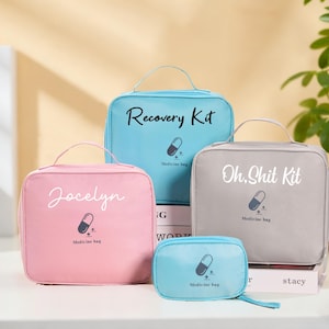 Puede incluir: Cuatro bolsas de medicamentos de varios tamaños y colores. Las bolsas son de color azul claro, rosa y gris, con texto blanco que dice "Recovery Kit", "Jocelyn" y "Oh, Shit Kit". Cada bolsa tiene un gráfico de píldora.