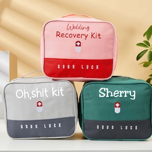 Puede incluir: Tres pequeñas bolsas cuadradas en rosa, gris y verde. La bolsa rosa dice "Wedding Recovery Kit" y la bolsa gris dice "Oh, shit kit". La bolsa verde tiene el nombre "Sherry". Cada bolsa tiene un asa y un símbolo médico.
