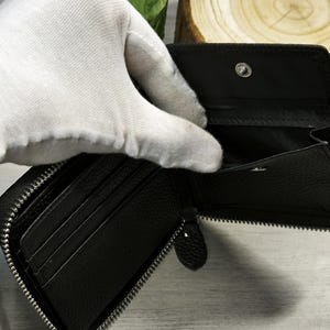 May include: Black, zipped wallet with several card slots and a coin pocket. The wallet is made of textured leather and has a silver zip. The interior is black. The wallet is open, showing the inside.