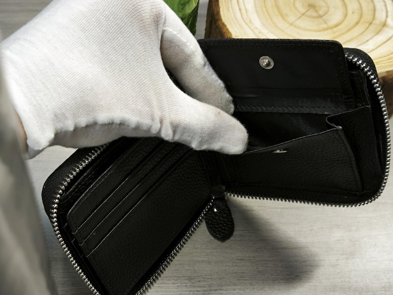 May include: Black, zipped wallet with several card slots and a coin pocket. The wallet is made of textured leather and has a silver zip. The interior is black. The wallet is open, showing the inside.