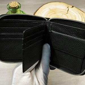 May include: Open black leather wallet with multiple compartments, including card slots and a coin pocket. The wallet has a full zip closure and a textured surface. The wallet is open, revealing the interior.
