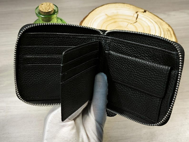 May include: Open black leather wallet with multiple compartments, including card slots and a coin pocket. The wallet has a full zip closure and a textured surface. The wallet is open, revealing the interior.