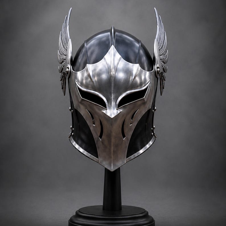 May include: A black and silver helmet featuring a pointed faceplate with elongated eye openings and stylized wing attachments on both sides. The helmet has a smooth, polished metallic finish on the front section and a dark, rounded dome structure.