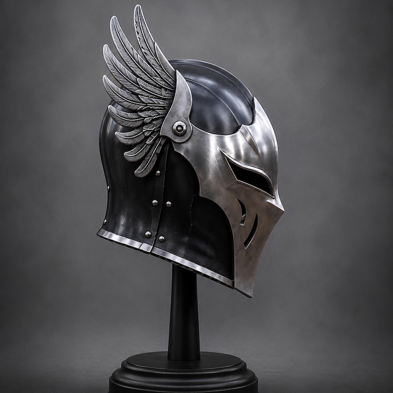 May include: A black metal helmet featuring a polished silver faceplate with narrow eye slits and a prominent silver wing attachment on the side. The helmet is constructed with visible rivets along the side and is displayed on a black stand.