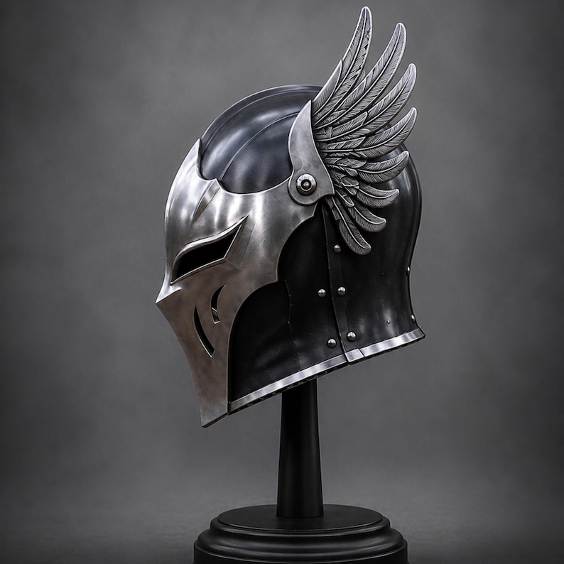 May include: A metallic helmet featuring a dark, smooth finish and a silver-toned faceplate with angular cutouts. The helmet is adorned with a prominent, detailed silver wing attachment on the side, secured with a visible rivet, and a silver trim.