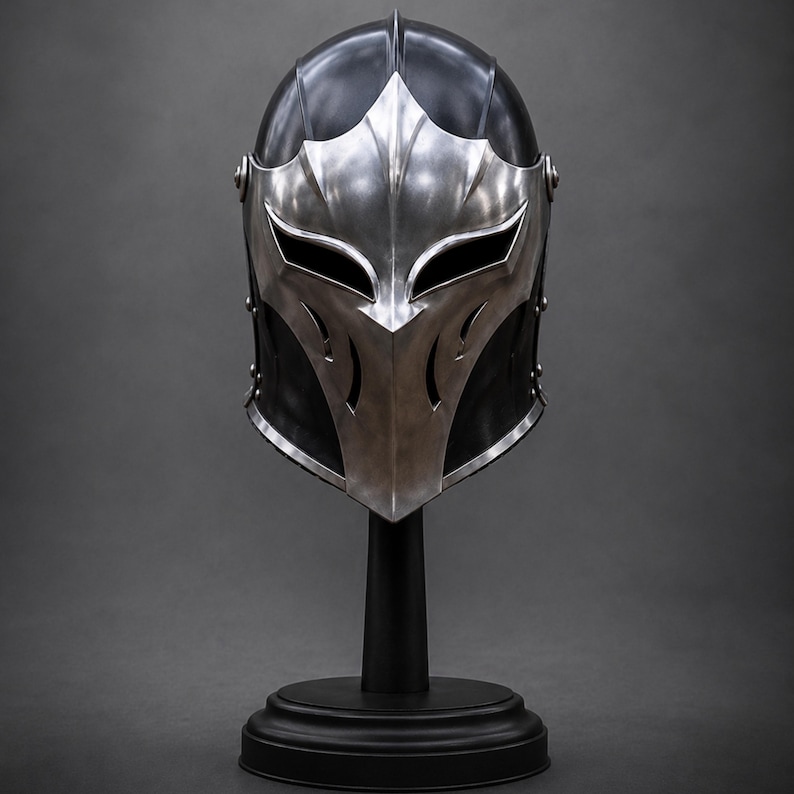May include: A black and silver metal helmet featuring a pointed, stylized faceplate with two wide, almond-shaped eye openings and vertical ventilation slits. The helmet is constructed with a smooth, polished finish and secured with visible rivets.
